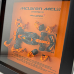 Framed three-dimensional artwork depicting the McLaren MCL38 with pit-crew figures