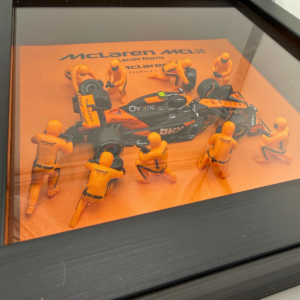 Framed three-dimensional artwork depicting the McLaren MCL38 with pit-crew figures