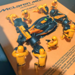 Framed three-dimensional artwork depicting the McLaren MCL38 with pit-crew figures