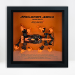 Framed three-dimensional artwork depicting the McLaren MCL38 with pit-crew figures