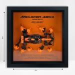Framed three-dimensional artwork depicting the McLaren MCL38 with pit-crew figures